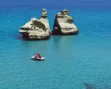 Due faraglioni bianchi emergono dal mare cristallino, con una pedalò che naviga vicino alla spiaggia dell'orso.