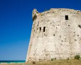 Antica torre mozza, con merli frastagliati, si erge contro un cielo blu intenso, testimone silenzioso di antiche storie.