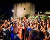Festa con gente che alza le mani davanti a una torre antica, tipica delle sagre Salento agosto.