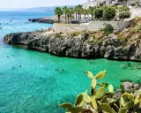 Splendida baia pugliese con acque cristalline e scogliere rocciose. Gente che nuota e si gode il sole, un vero paradiso per chi ama il **puglia mare**.