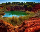 Un suggestivo lago di bauxite in Puglia, con acque verdi smeraldo circondate da rocce rosse e vegetazione lussureggiante.