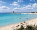 Spiaggia Scala di Furno con torre antica e acque turchesi. Persone si godono il sole e il mare cristallino.