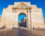Porta Napoli, un arco trionfale in pietra leccese, invita a scoprire le cose da fare a Lecce. Un'antica porta che segna l'ingresso alla città barocca.