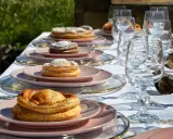 Tavola apparecchiata con bicchieri di cristallo e piatti rosa, su cui riposano dolci invitanti, tra cui una piscialetta leccese cosparsa di zucchero a velo.