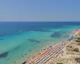 Spiaggia affollata con ombrelloni colorati e acque cristalline, le Maldive della Puglia dove si trovano per godersi il sole e il mare.