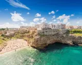 Un borgo bianco su scogliere a picco sul mare turchese, una spiaggia affollata e un invito a scoprire la Puglia da visitare.