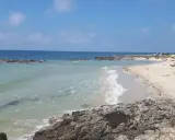 Spiaggia con scogli e mare cristallino, tipica delle calette puglia. Persone in acqua e sulla sabbia, ombrelloni e lettini.