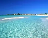 Acque cristalline lambiscono spiagge bianche, con un villaggio sullo sfondo sotto un cielo azzurro intenso.