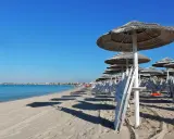 Ombrelloni di paglia e lettini bianchi sul lungomare Torre Lapillo, con il mare azzurro e il cielo limpido.