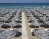 Filettato di ombrelloni di paglia e lettini sulla sabbia dorata, con il mare azzurro sullo sfondo. Un paradiso a Presicce Lido Marini.