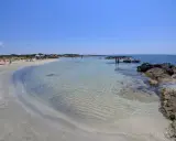Spiaggia di sabbia bianca e mare cristallino a Marina di Salve, con scogli e persone che si godono il sole.
