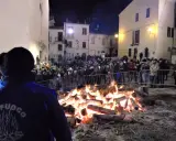 Grande falò nella piazza per la festa della birra Sant'Antonio Abate. La folla ammira le fiamme mentre un gruppo suona musica.