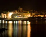 Otranto di notte: luci, castello e riflessi sull'acqua. La città si anima, pronta per le discoteche estive.