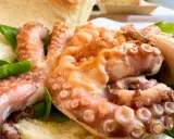 Tentacoli di polpo succulenti, un assaggio della sagra del polpo a Melendugno, serviti con pane croccante e foglie verdi.