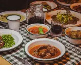 Tavola imbandita in una trattoria tipica salentina con vari piatti di carne e contorni, accompagnati da vino rosso.