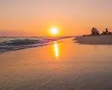 Tramonto dorato sulla spiaggia di Ugento, Salento. Famiglie rilassate sulla sabbia mentre il sole si specchia sul mare calmo.