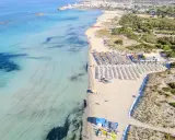Spiaggia di Torre San Giovanni con ombrelloni e lettini, mare cristallino e vegetazione mediterranea.