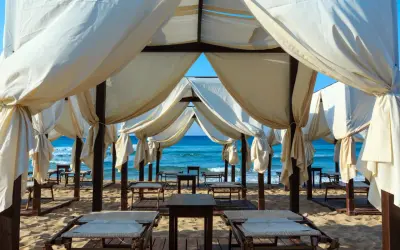 Tende bianche su una spiaggia dorata, con il mare azzurro sullo sfondo. Un angolo di paradiso che ricorda le Maldive del Salento, pronto per il relax.