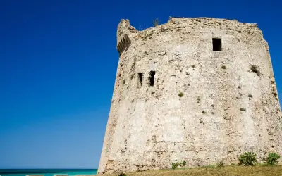Antica torre mozza, con merli frastagliati, si erge contro un cielo blu intenso, testimone silenzioso di antiche storie.