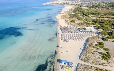 Spiaggia di Torre San Giovanni con ombrelloni e lettini, mare cristallino e vegetazione mediterranea.