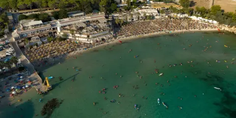 Vista aerea di una spiaggia affollata con ombrelloni e persone che nuotano nel mare cristallino, una delle spiagge più belle del mare di Taranto.