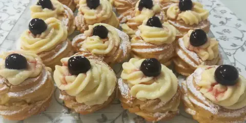 Zeppole pugliesi, dolci fritti con crema pasticcera e ciliegina, spolverati di zucchero a velo.