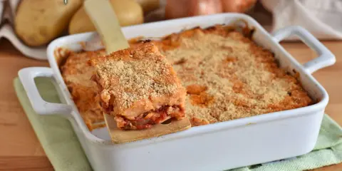 Una fetta di focaccia di patate ripiena pugliese dorata e croccante, servita da una teglia bianca.