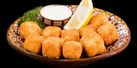 Croccanti cubetti di ricotta fritta salentina dorati, serviti su un piatto decorato con limone, salsa bianca e aneto.