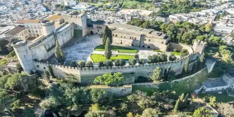 Castello normanno con torri rotonde e mura merlate, ideale per scoprire dove andare a Pasquetta in Puglia, circondato da verde e un borgo.