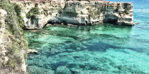 Scogliere bianche e acque cristalline, un paradiso tra le spiagge Puglia. Nuotatori si godono il mare turchese.