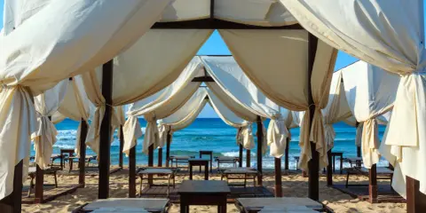Tende bianche su una spiaggia dorata, con il mare azzurro sullo sfondo. Un angolo di paradiso che ricorda le Maldive del Salento, pronto per il relax.