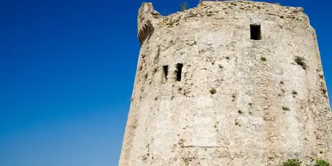 Antica torre mozza, con merli frastagliati, si erge contro un cielo blu intenso, testimone silenzioso di antiche storie.