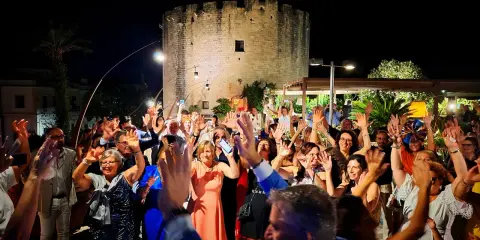 Festa con gente che alza le mani davanti a una torre antica, tipica delle sagre Salento agosto.