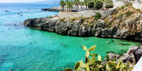 Splendida baia pugliese con acque cristalline e scogliere rocciose. Gente che nuota e si gode il sole, un vero paradiso per chi ama il **puglia mare**.