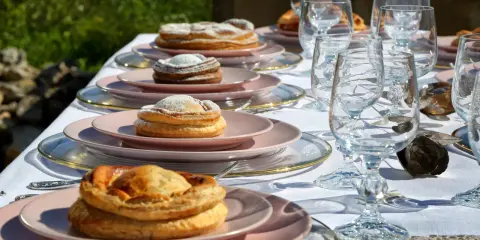 Tavola apparecchiata con bicchieri di cristallo e piatti rosa, su cui riposano dolci invitanti, tra cui una piscialetta leccese cosparsa di zucchero a velo.