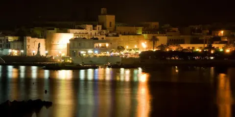 Otranto di notte: luci, castello e riflessi sull'acqua. La città si anima, pronta per le discoteche estive.