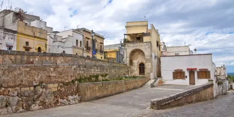 Antica strada di Ugento, dove si trova questo scorcio di case storiche con un muro in pietra grezza e un arco in tufo.