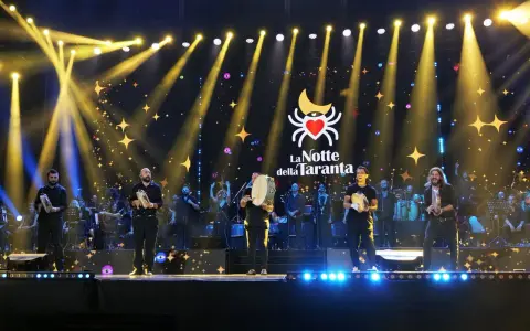 Artisti sul palco con tamburelli, orchestra e luci scintillanti per la sagra della taranta.
