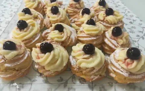 Zeppole pugliesi, dolci fritti con crema pasticcera e ciliegina, spolverati di zucchero a velo.