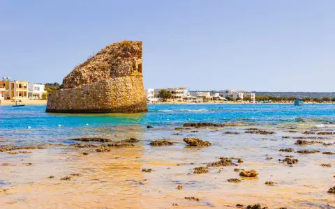La torre pali di Lido Marini, con il mare cristallino e le case bianche sullo sfondo, evoca un'estate senza fine.