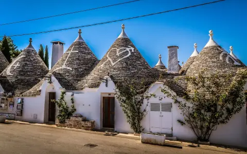 Trulli bianchi con tetti conici in pietra, un cuore disegnato su uno di essi, in un borgo tra i più belli d'Italia in Puglia.