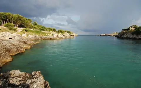 Baia rocciosa con acqua cristallina, alberi sulla costa. Un paesaggio che evoca i modi di dire salentini, come "fare la bella vita".