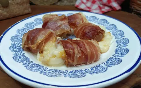 Involtini di interiora pugliesi avvolti in pancetta croccante, serviti su un piatto bianco con decorazioni blu.