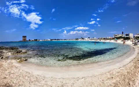 Spiaggia incantevole nel Salento ionico, con acque cristalline, sabbia dorata e un'antica torre di avvistamento.