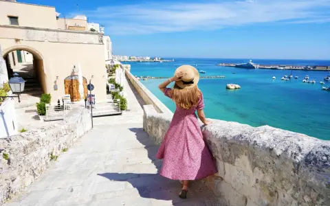 Una donna con cappello di paglia ammira il mare turchese e il porto di Otranto. Scopri cosa vedere in questo gioiello pugliese.