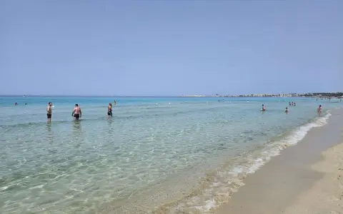 Persone in acqua cristallina vicino alla spiaggia di Gallipoli paese. Il mare calmo riflette il cielo azzurro.