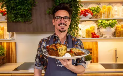 Chef sorridente con un piatto di torta salata, ispirata alle ricette leccesi, con pomodorini e basilico sullo sfondo.