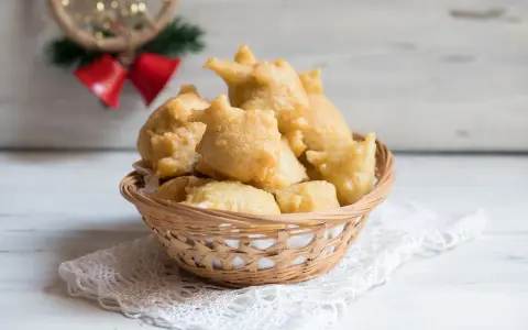 Cesto di pittula salentina dorata, un dolce fritto tipico delle feste, su un pizzo bianco.