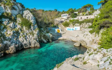 Baia incantevole con acque cristalline, perfetta per un tour Puglia 10 giorni. Case bianche e rocce a picco sul mare.