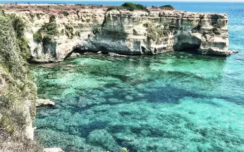 Scogliere bianche e acque cristalline, un paradiso tra le spiagge Puglia. Nuotatori si godono il mare turchese.